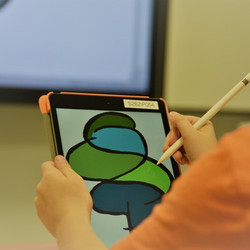 Kind hält ein iPad und ein Stift, im Hintergrund ist eine digitale Tafel zu sehen